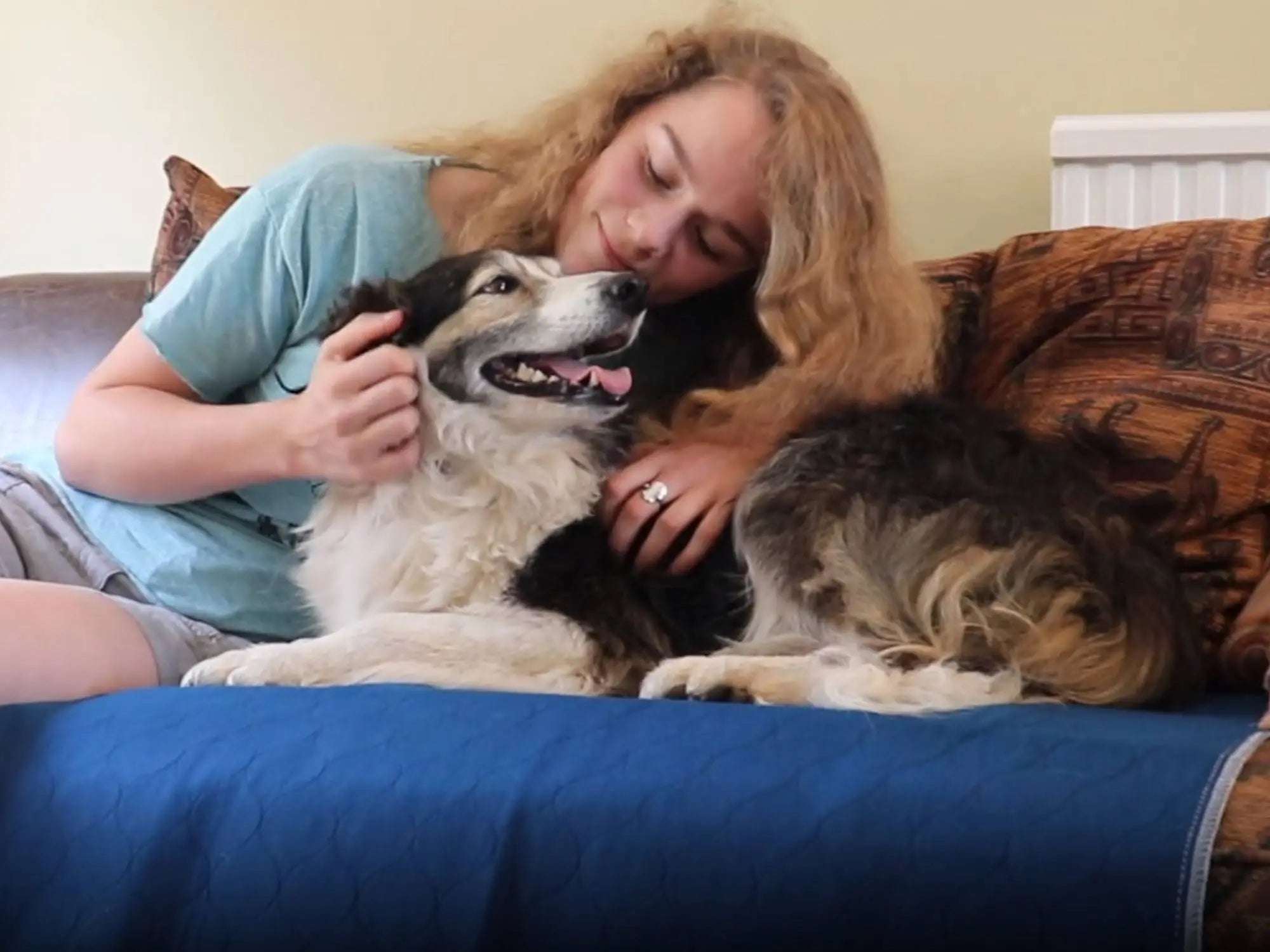 An image of a woman cuddling a dog, sat on a dog incontinence pad.