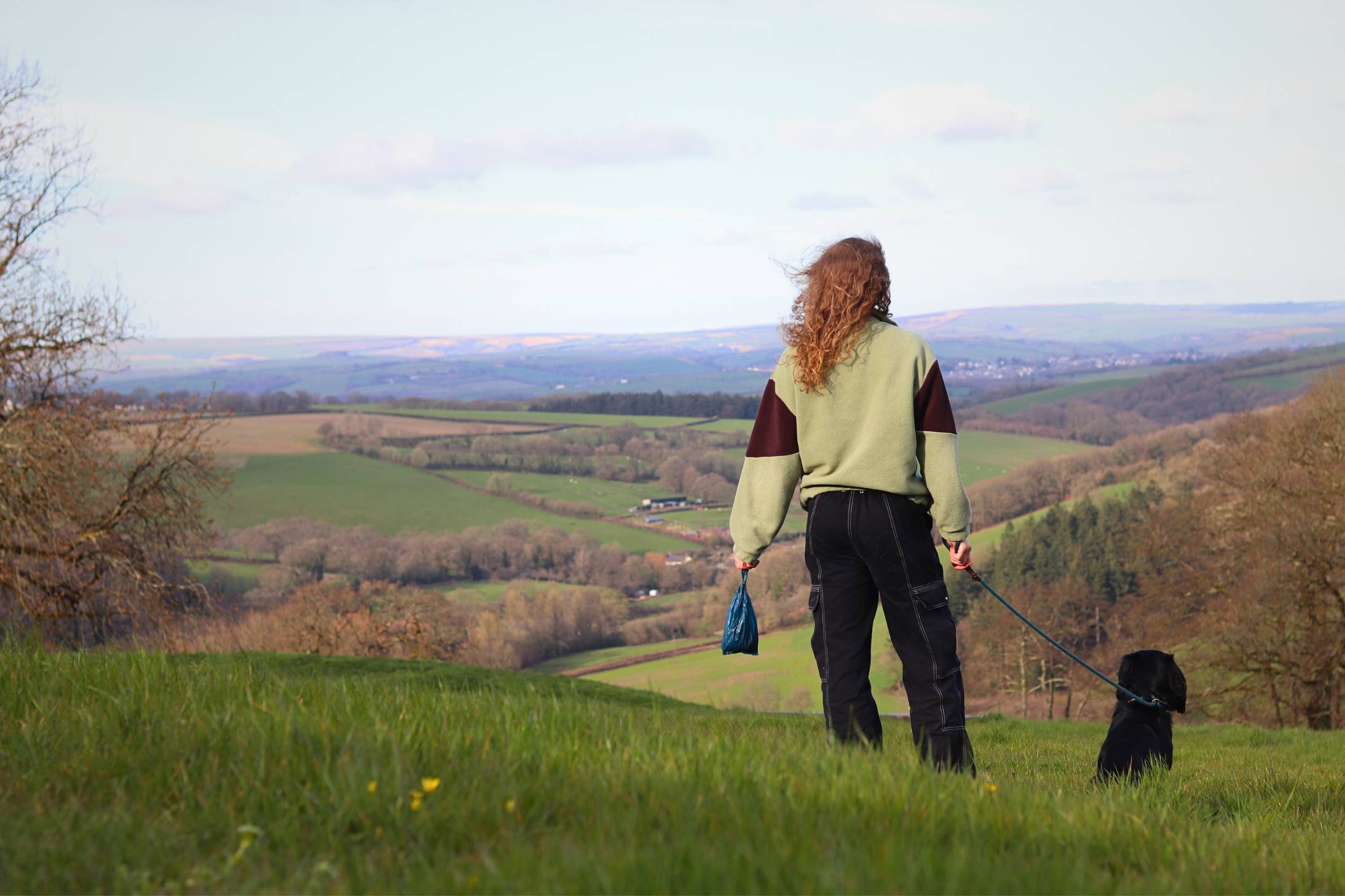 A photo of a woman and a dog looking out into the distance in a hilly, outdoor setting