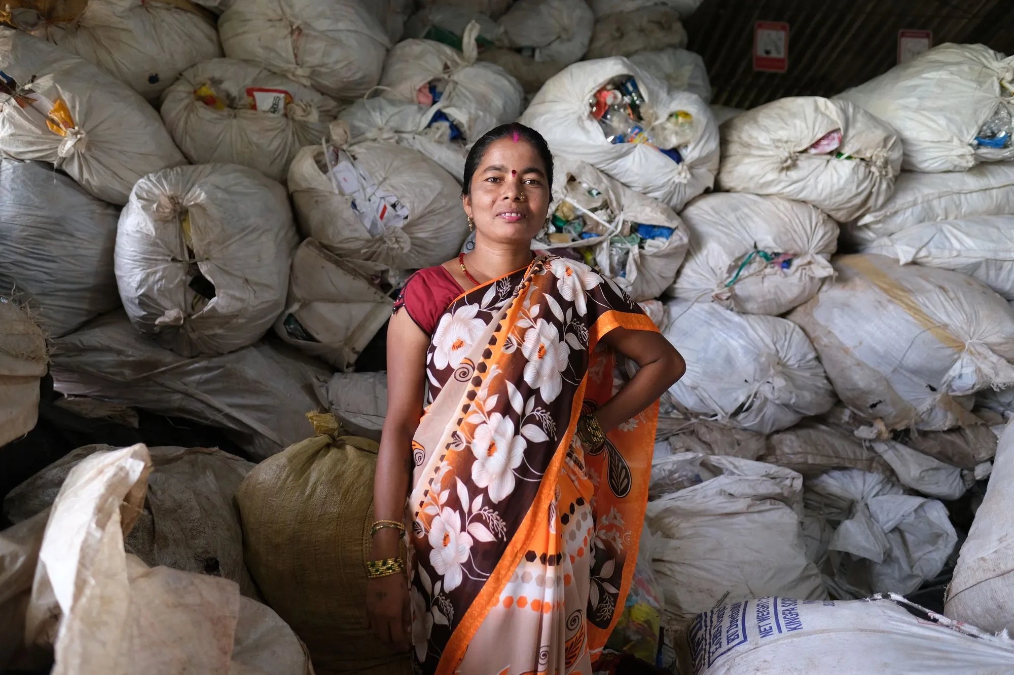An image of a woman standing in front of bags of collected plastic